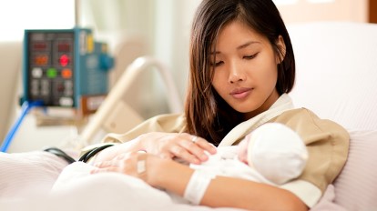 young Asian woman holds newborn in hospital bed
