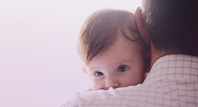 dark haired baby peeking over man's shoulder
