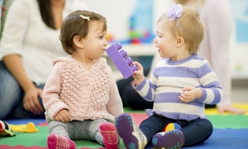 two girl toddlers wearing sweaters playing. one girl blond, other brown hair