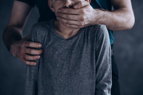 child with dirty clothes has an adult holding him, covering his mouth