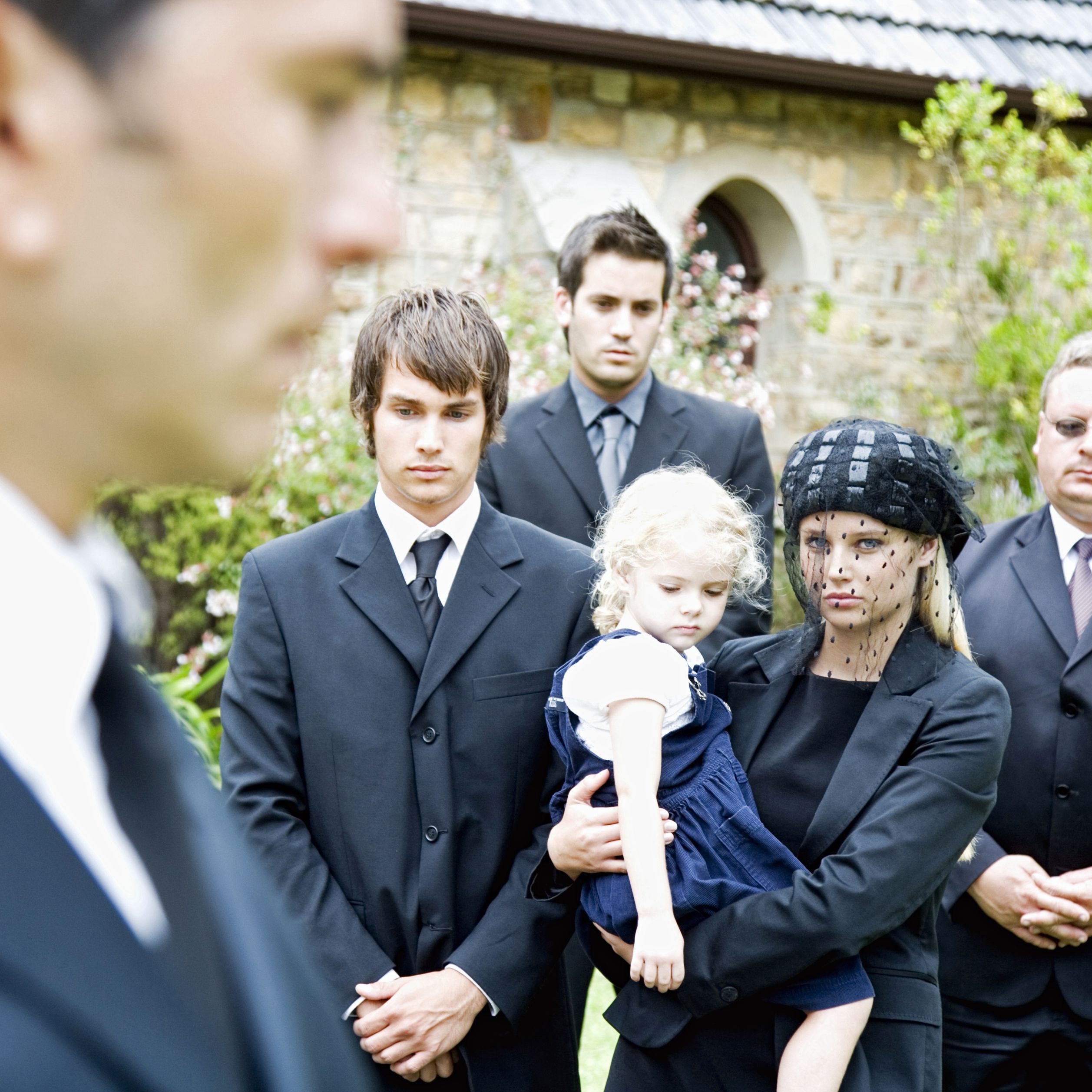 funeral. three boys in teens, early 20s, dressed in suits. blond teen girl holds little blonde girl